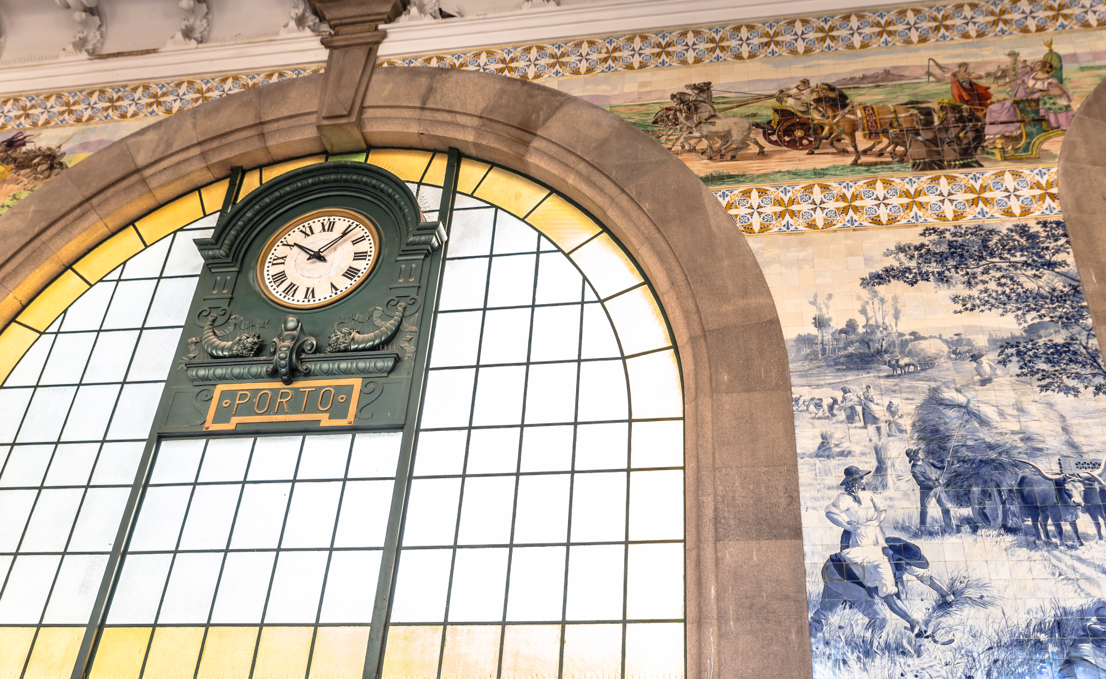 Historisk grønt ur på São Bento jernbanestation i Porto, Portugal, med traditionelle blå og hvide azulejo-fliser der viser historiske scener