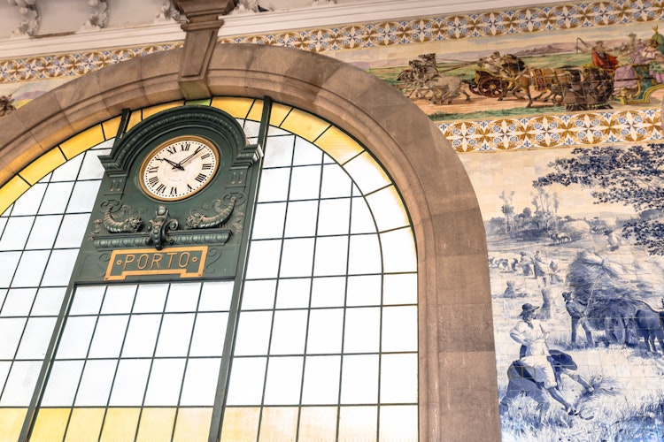 Historisk grønt ur på São Bento jernbanestation i Porto, Portugal, med traditionelle blå og hvide azulejo-fliser der viser historiske scener