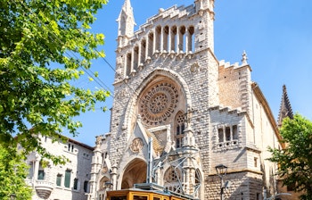 Den ikoniske gul-røde sporvogn fra 1913 foran Sant Bartomeu kirken på Plaça de la Constitució i Soller, Mallorca - en populær turistattraktion og del af den historiske Tren de Soller