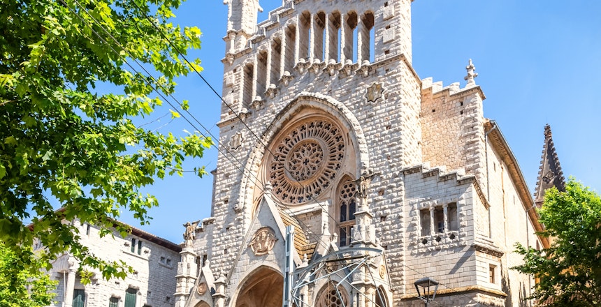 Den ikoniske gul-røde sporvogn fra 1913 foran Sant Bartomeu kirken på Plaça de la Constitució i Soller, Mallorca - en populær turistattraktion og del af den historiske Tren de Soller