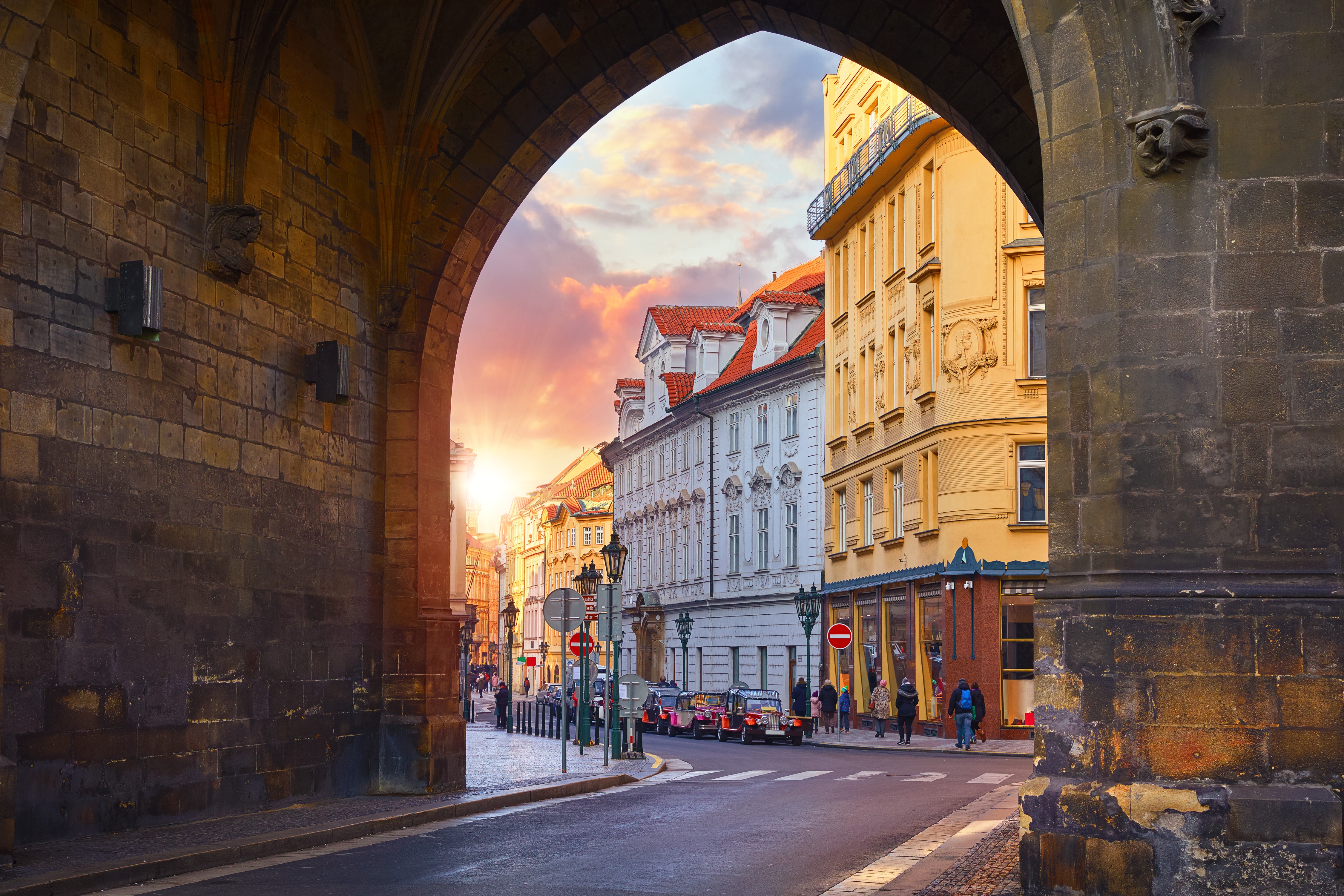 Historisk stenport indramme farverige europæiske bygninger i barok stil under gyldent solnedgangslys