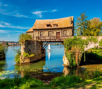 Historisk bindingsværk vandmølle over Seine-floden i Vernon, Normandiet med grønne omgivelser og blå himmel