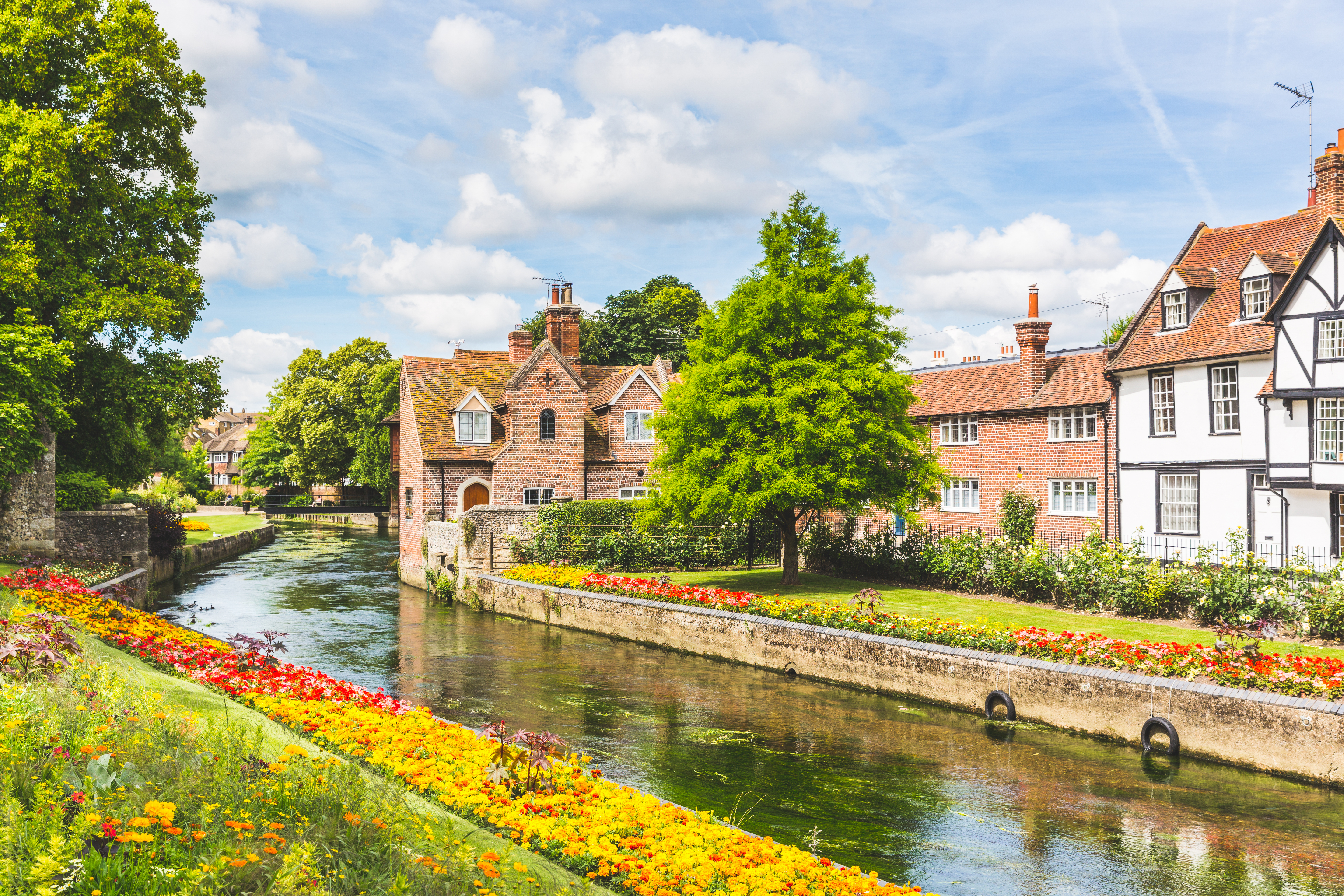 Idyllisk udsigt over historiske bygninger langs kanalen i Canterbury, England med farverige blomster og traditionel arkitektur på en solrig sommerdag