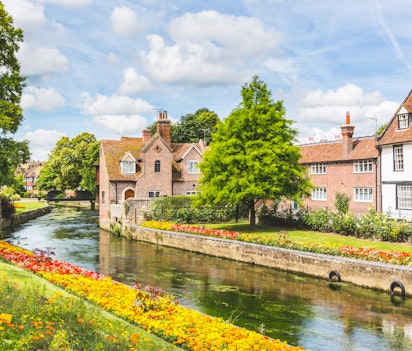 Idyllisk udsigt over historiske bygninger langs kanalen i Canterbury, England med farverige blomster og traditionel arkitektur på en solrig sommerdag