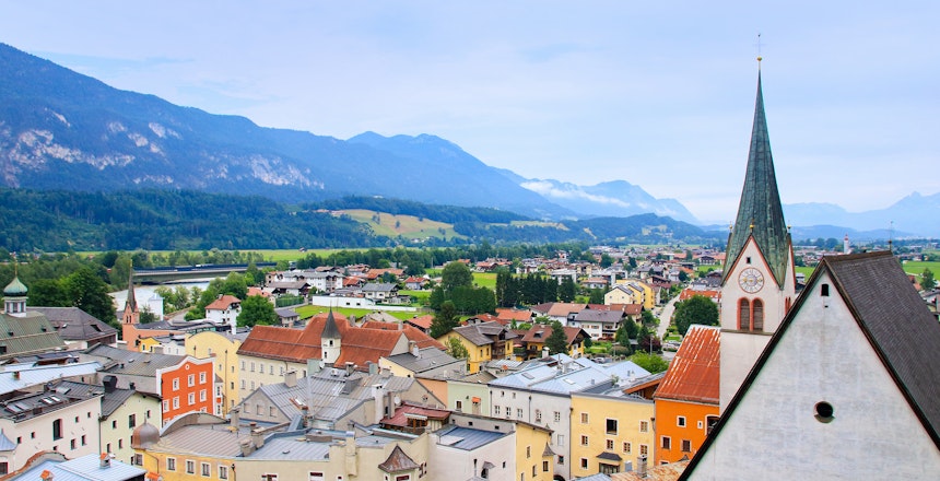 Panoramaudsigt over den historiske middelalderby Rattenberg i Tyrol, Østrig, med farverige bygninger, kirketårn og omgivet af de majestætiske alper under en blå sommerhimmel