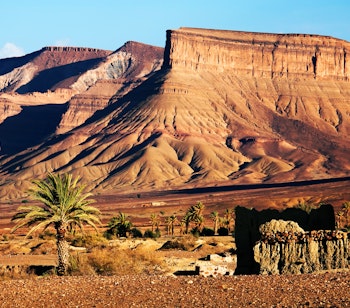Ældgamle stenruiner med de majestætiske Atlasbjerge som baggrund i Marokko, et vidnesbyrd om landets rige historie midt i det barske ørkenlandskab