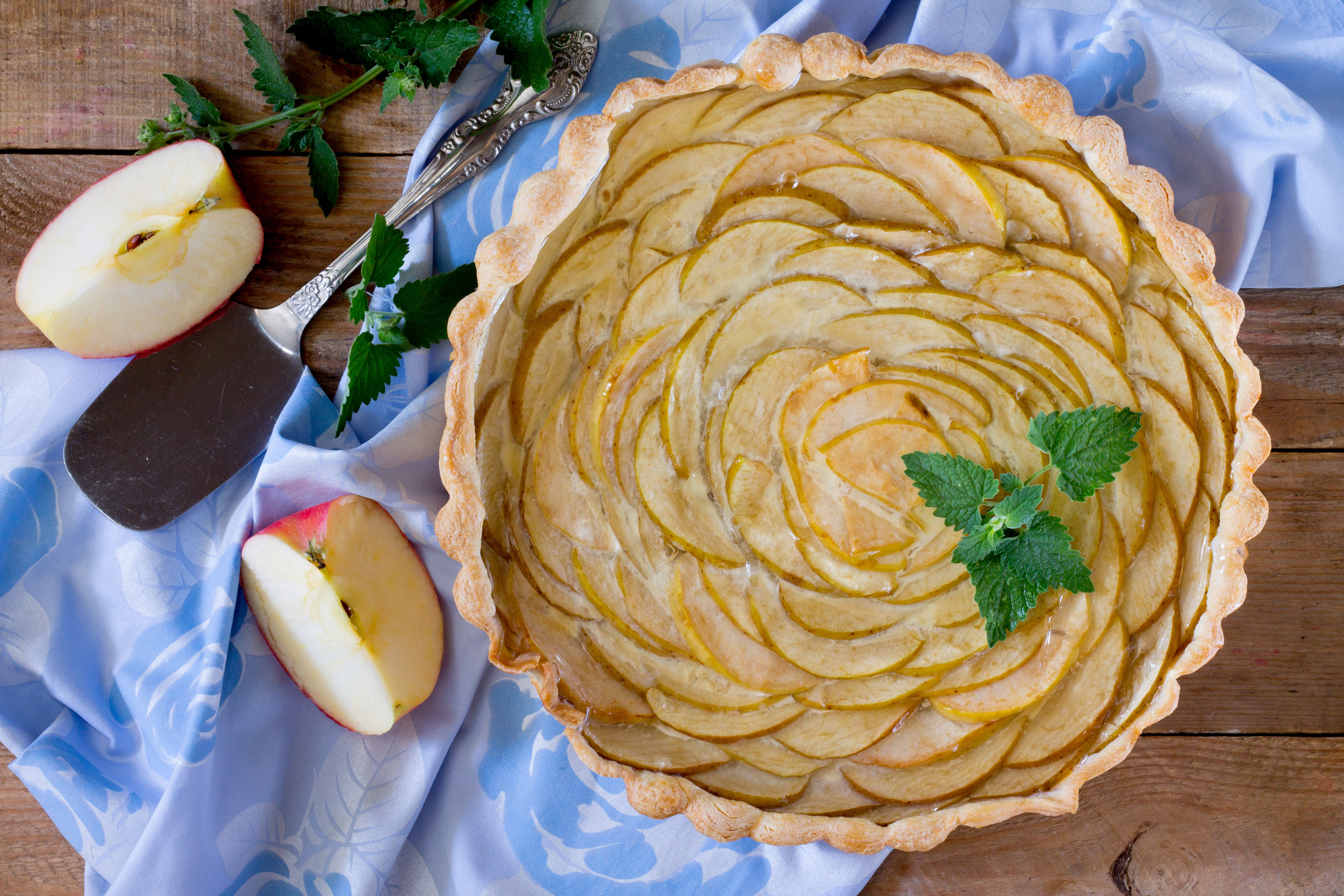 Hjemmelavet æbletærte med flot mønster af æbleskiver, serveret på rustikt træbord med friske mynteblade og halve æbler