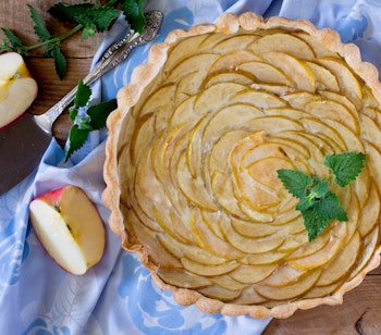 Hjemmelavet æbletærte med flot mønster af æbleskiver, serveret på rustikt træbord med friske mynteblade og halve æbler