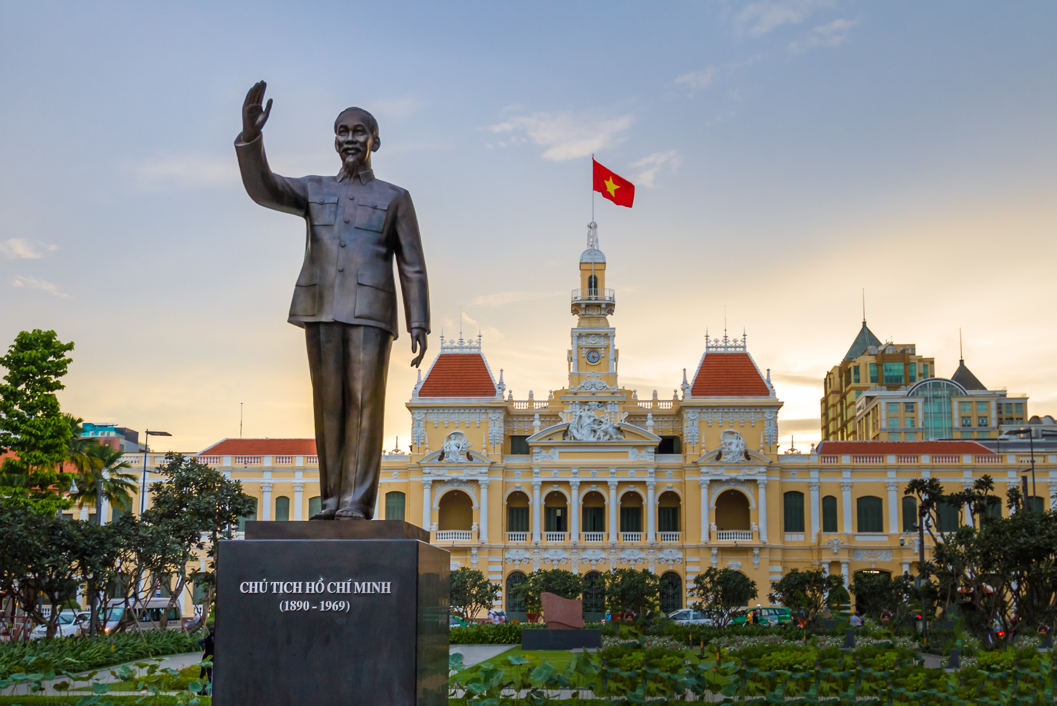 Ho Chi Minh statue foran byhuset i Saigon Vietnam med vietnamesisk flag