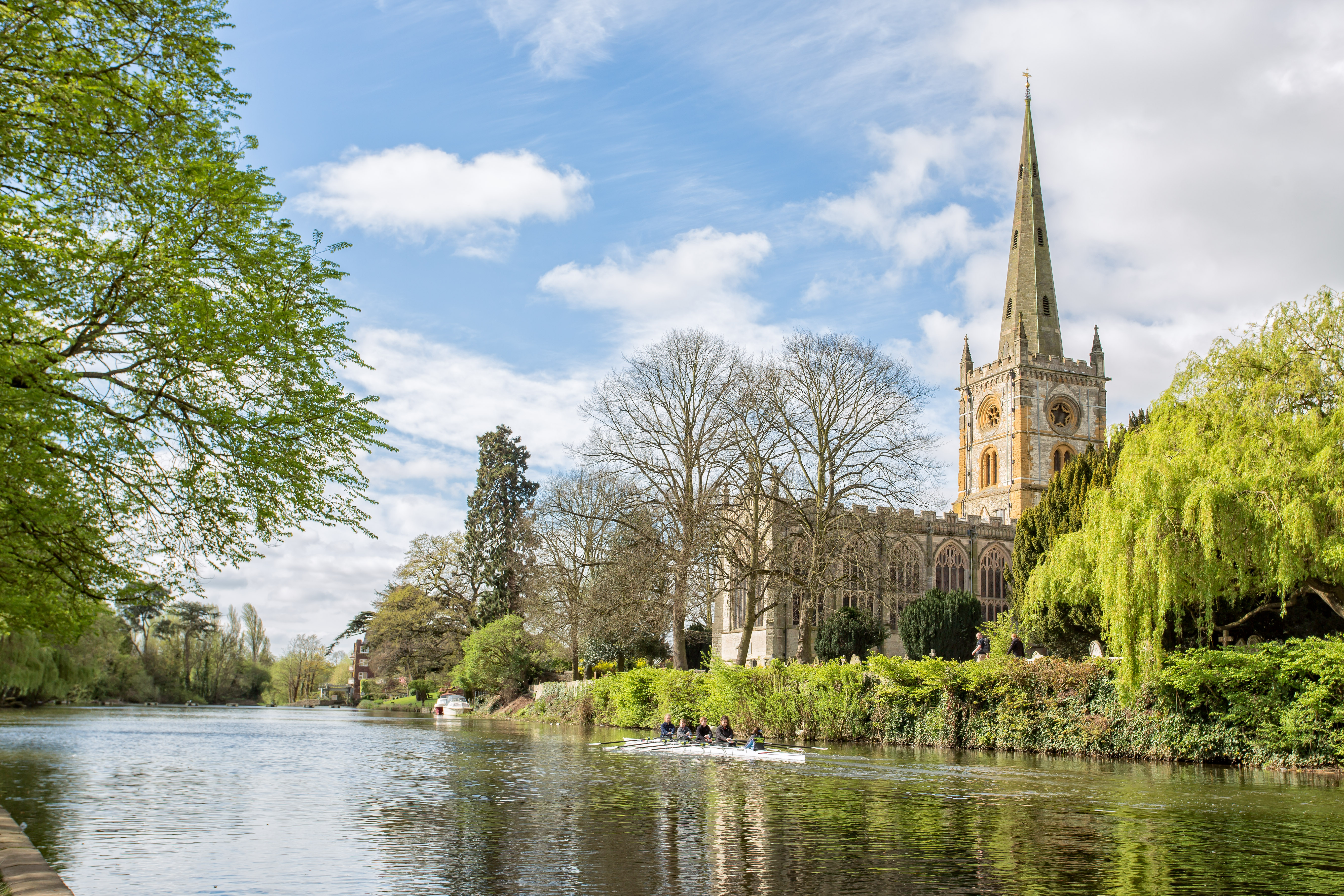 Holy Trinity Church spejler sig i floden Avon i Stratford-upon-Avon, England, med en robåd på det rolige vand en solrig forårsdag