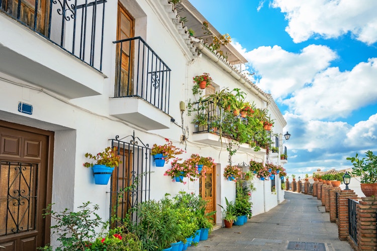 Malerisk smal gade med traditionelle hvide huse prydet med blå blomsterkrukker i Mijas landsby, Andalusien