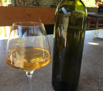 Glas hvidvin og flaske på udendørs restaurantterrasse i Middelhavet