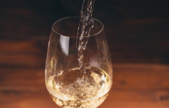 Hvidvin der hældes fra flaske i elegante vinglas på rustik træbaggrund, perfekt til gourmetrejser