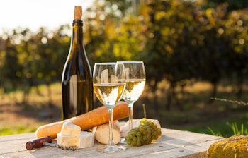 To glas hvidvin med ost og baguette ved solnedgang i en idyllisk vingård - perfekt til en gastronomisk ferieoplevelse