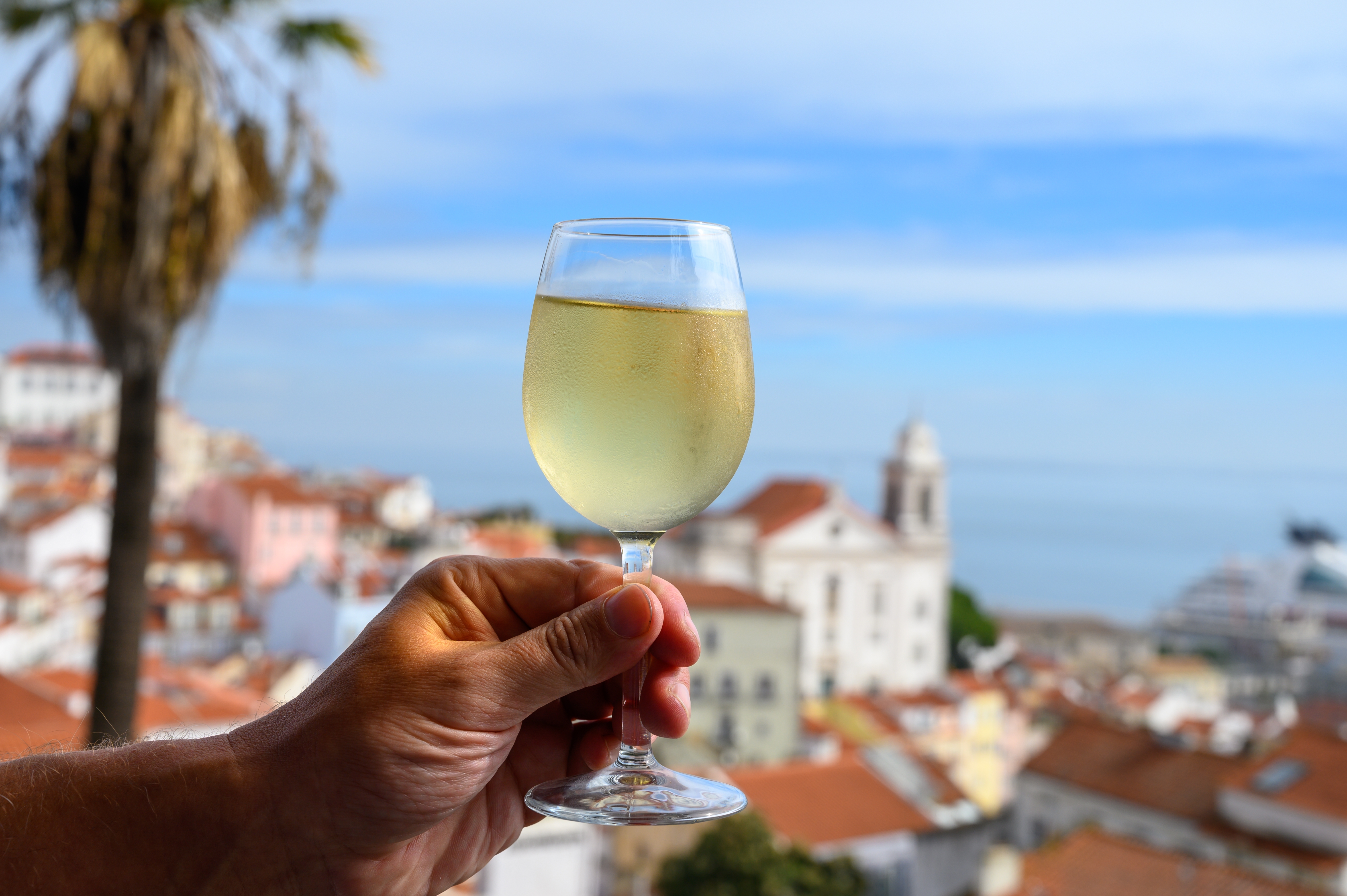 Hånd med glas hvidvin på udendørs café med udsigt over den farverige gamle bydel i Lissabon, Portugal