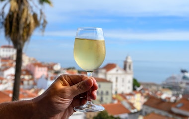 Hånd med glas hvidvin på udendørs café med udsigt over den farverige gamle bydel i Lissabon, Portugal