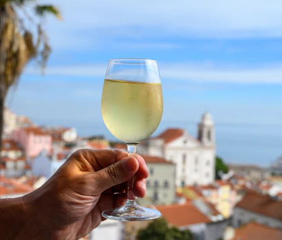 Hånd med glas hvidvin på udendørs café med udsigt over den farverige gamle bydel i Lissabon, Portugal