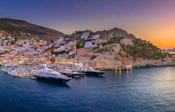 Betagende udsigt over Hydras maleriske havn med traditionelle hvide bygninger på bjergsiden og både fortøjet i det azurblå Ægæerhav