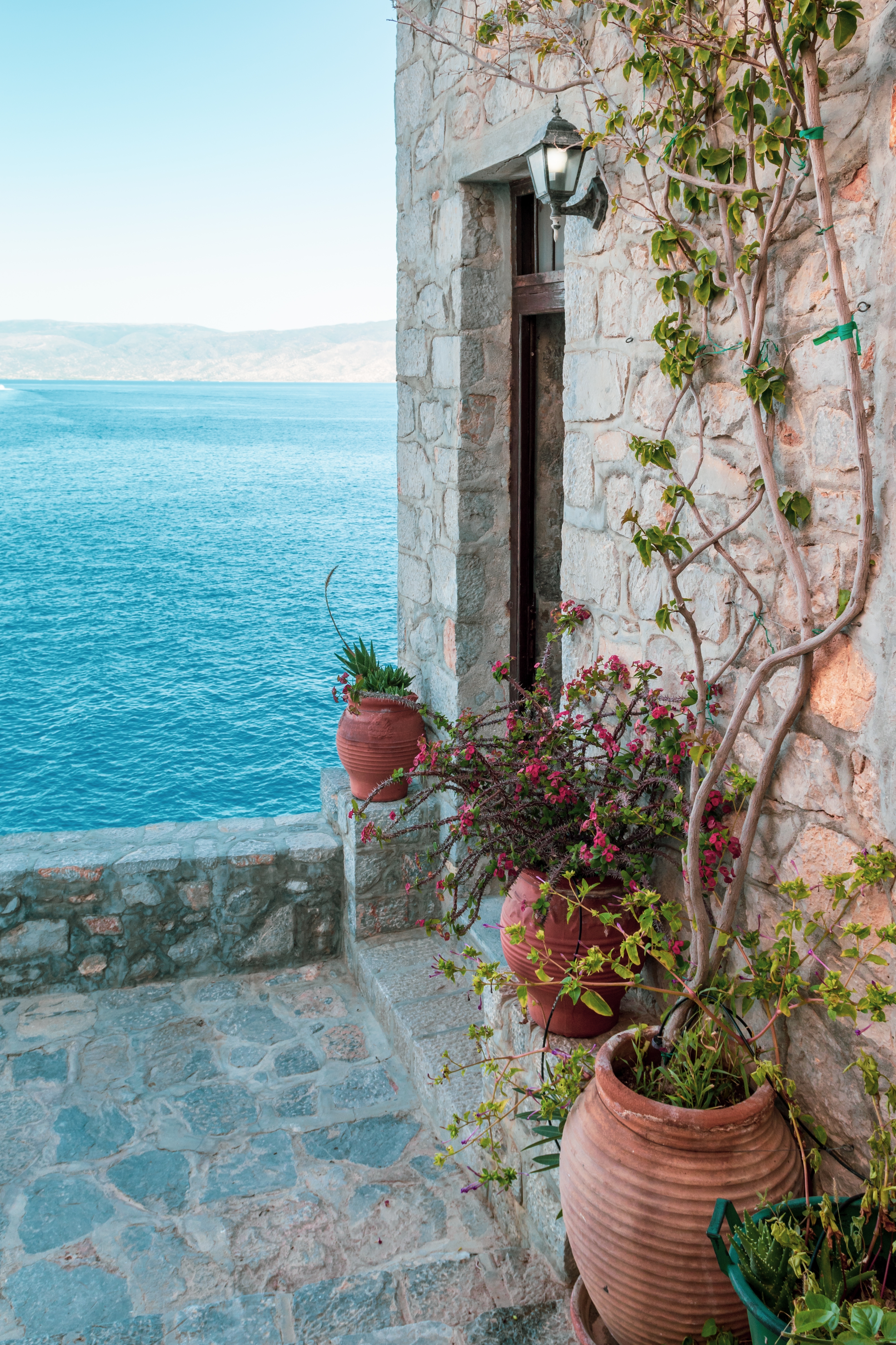 Idyllisk terrasse med terrakottakrukker og klatreplanter med udsigt over det blå Ægæiske Hav på Hydra-øen i Grækenland