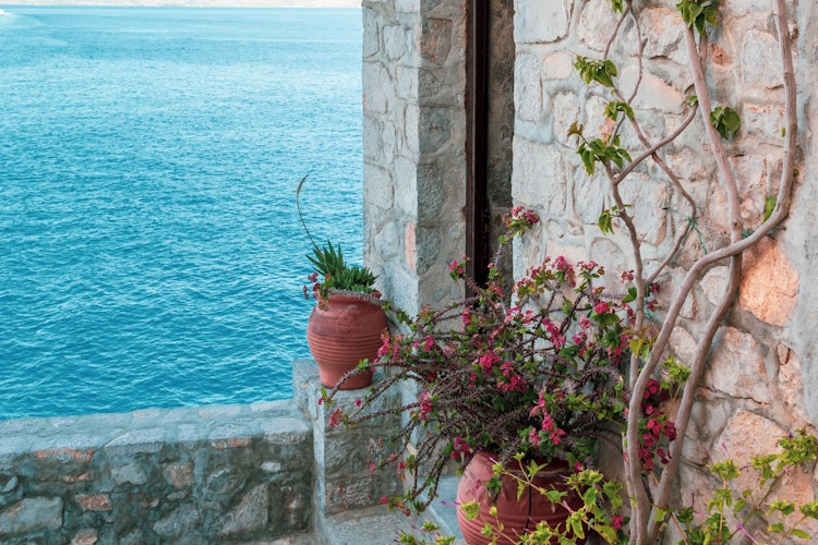 Idyllisk terrasse med terrakottakrukker og klatreplanter med udsigt over det blå Ægæiske Hav på Hydra-øen i Grækenland