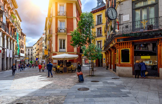Charmerende gammel brostensbelagt gade i Madrids historiske centrum med traditionelle bygninger, farverige balkoner og hyggelige caféer