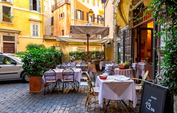 Charmerende gammel gade i Rom med hyggelig italiensk restaurant og udendørs terrasse omgivet af historisk arkitektur og grønne planter