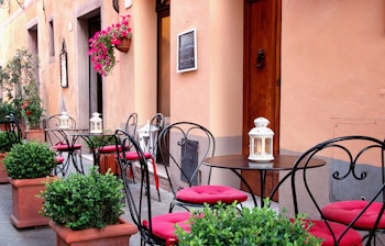 Hyggelig traditionel italiensk café med udendørs siddepladser i en malerisk gade i Toscana, med rustikke borde og stole omgivet af potteplanter