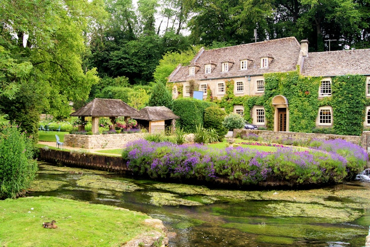 Charmerende havelandskab i Bibury landsbyen i Cotswolds, England med traditionelle stenhuse, farverige blomster og rislende vandløb