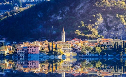 Charmerende landsby med farverige bygninger spejler sig i Como-søens blå vand med majestætiske bjerge i baggrunden, Italien