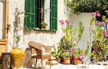 Charmerende gårdhave med flettestol, grønne skodder og farverige blomster i krukker ved et traditionelt hus i Mallorca, Spanien