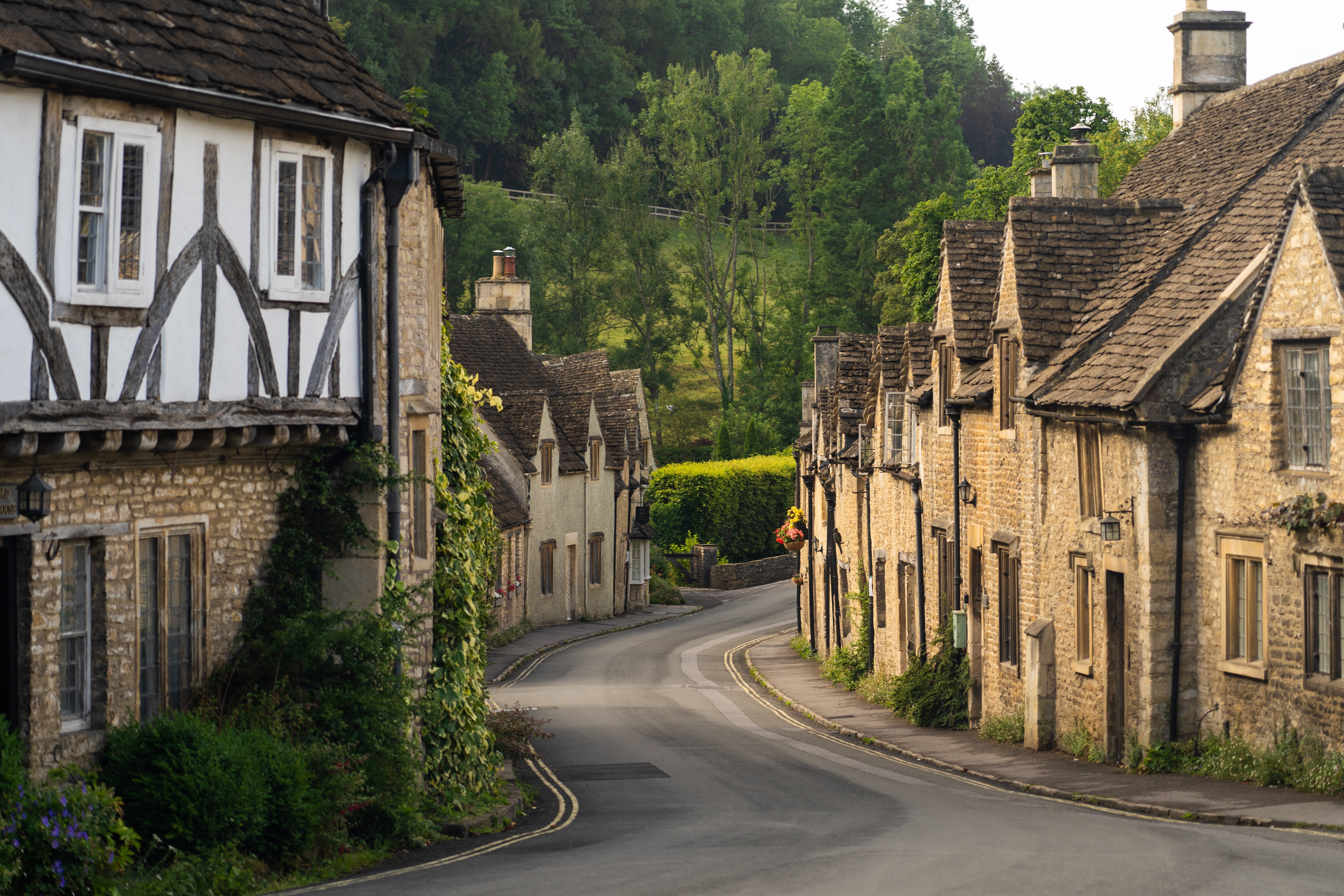 Charmerende landsbygade i Castle Combe i Cotswolds, England, med historiske stenhuse og bindingsværksbygninger langs den snoede vej