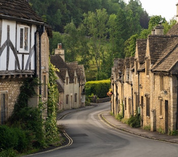 Charmerende landsbygade i Castle Combe i Cotswolds, England, med historiske stenhuse og bindingsværksbygninger langs den snoede vej