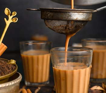 Traditionel indisk masala chai te hældes fra kande med duftende krydderier på mørkt bord - en autentisk smagsoplevelse på rejser til Indien