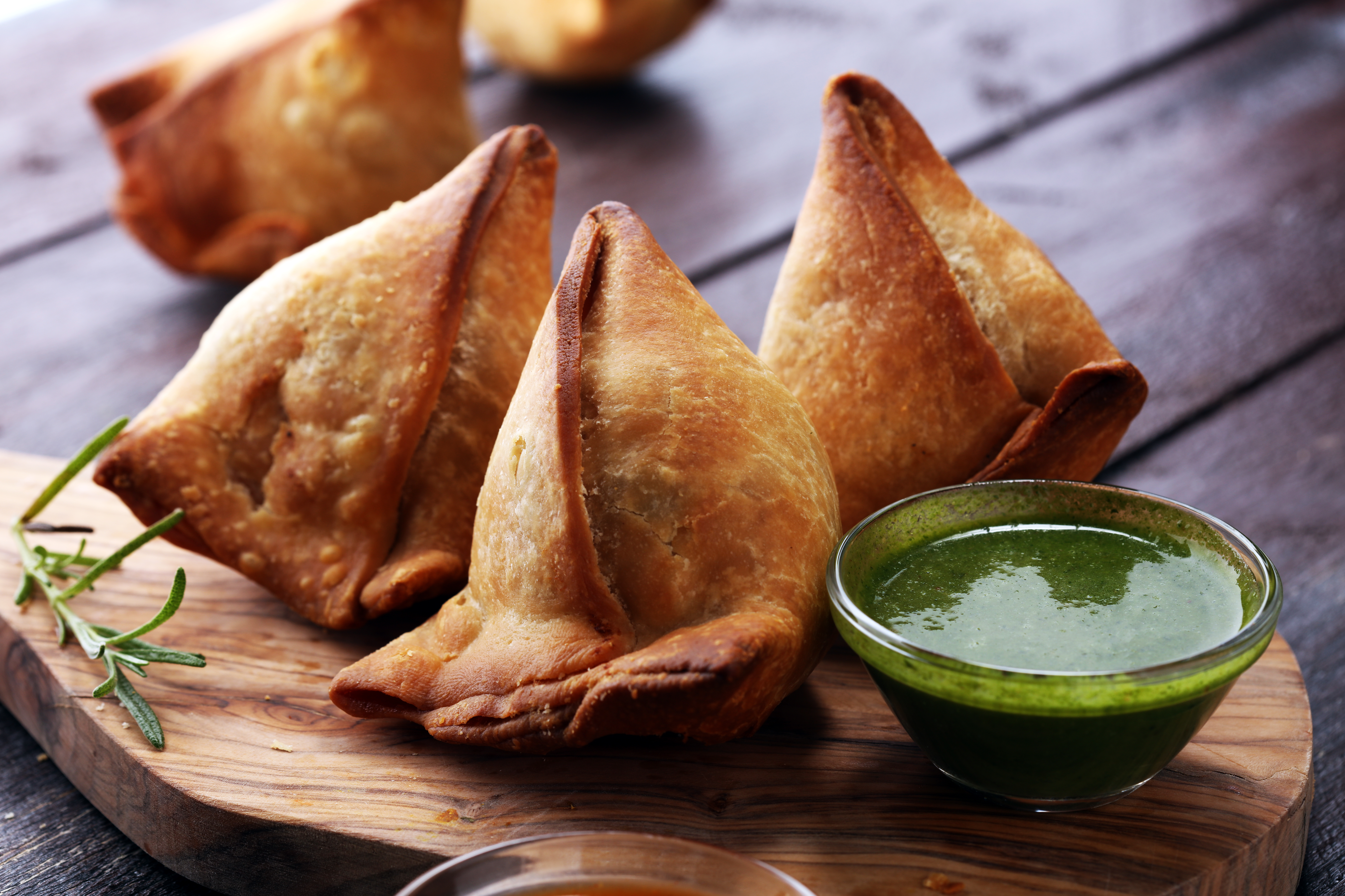 Gyldne indiske samosas med grøn chutney serveret på træbræt - traditionel vegetarisk streetfood fra Punjab-regionen
