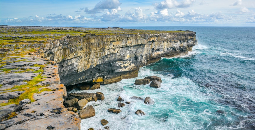 Dramatiske kalkstensklipper på Inishmore med turkisblåt Atlanterhav og brusende bølger langs den barske kystlinje på Aran-øerne i Irland