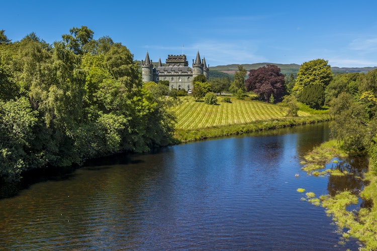 Inveraray Castle med gotisk arkitektur spejlet i Loch Fyne omgivet af grønne områder i Argyll, Skotland