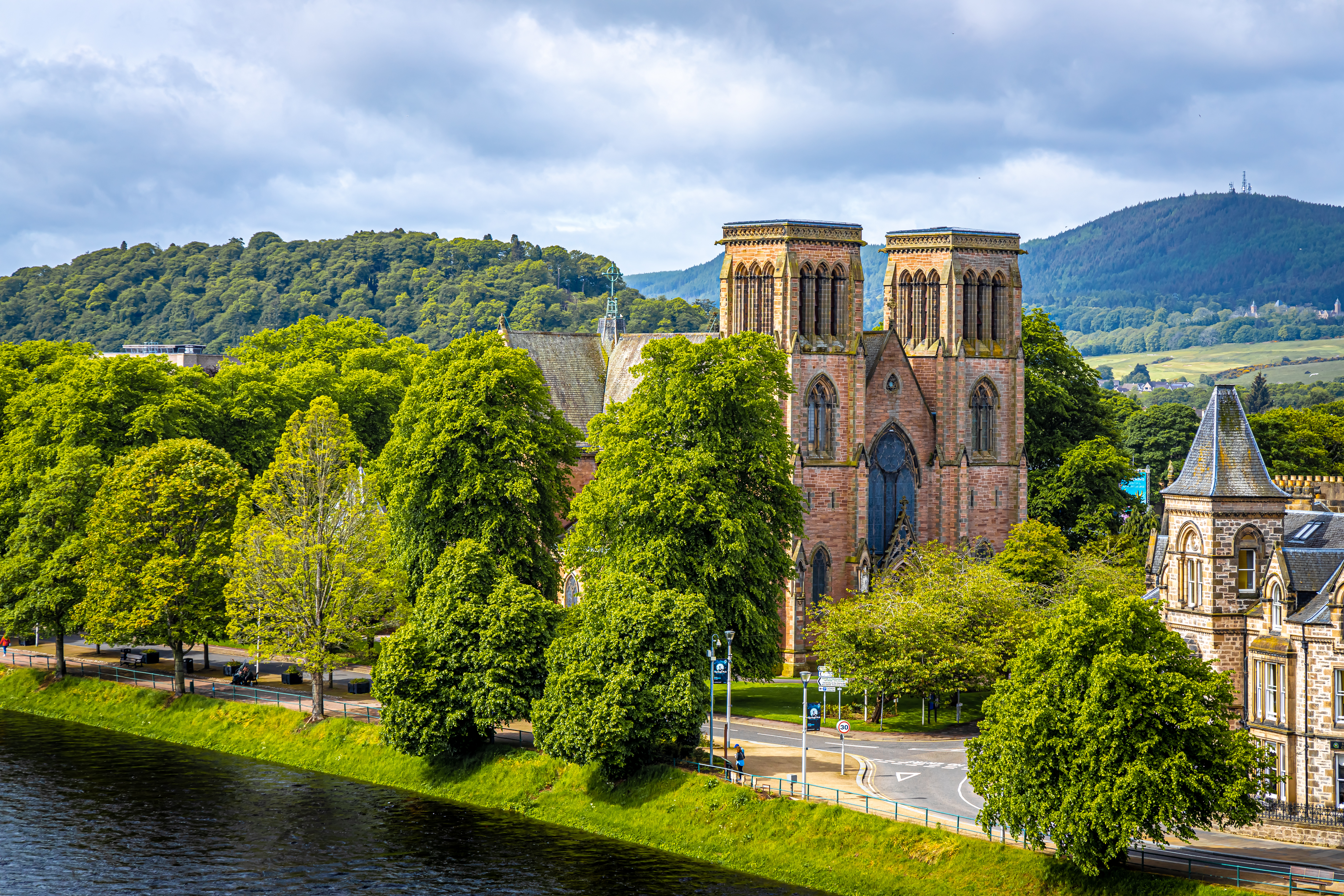 Inverness Katedral ved River Ness med grønne træer og skotske højlande i baggrunden