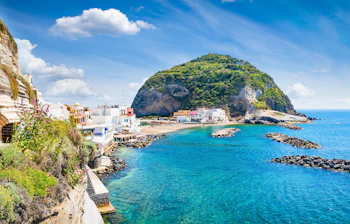 Smuk kystlandsby på Ischia med tyrkisblåt vand og grøn ø i baggrunden Italien