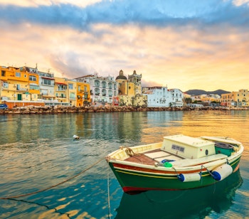 Malerisk solnedgang over Ischia med farverige bygninger langs havnefronten og gyldent lys reflekteret i Middelhavet nær Napoli