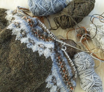 Traditionel islandsk lopapeysa sweater under strikning med farvede garnnøgler og strikkepinde, symboliserer Islands håndværkstraditioner