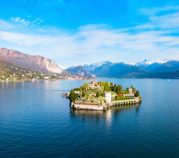 Betagende luftfoto af Isola Bella øen med det barokke palads og haver i Lago Maggiore søen, med Stresa by og de italienske alper i baggrunden
