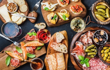 Italiensk antipasti-anretning med parmaskinke, oste, bruschetta, oliven og rødvin serveret på mørk baggrund