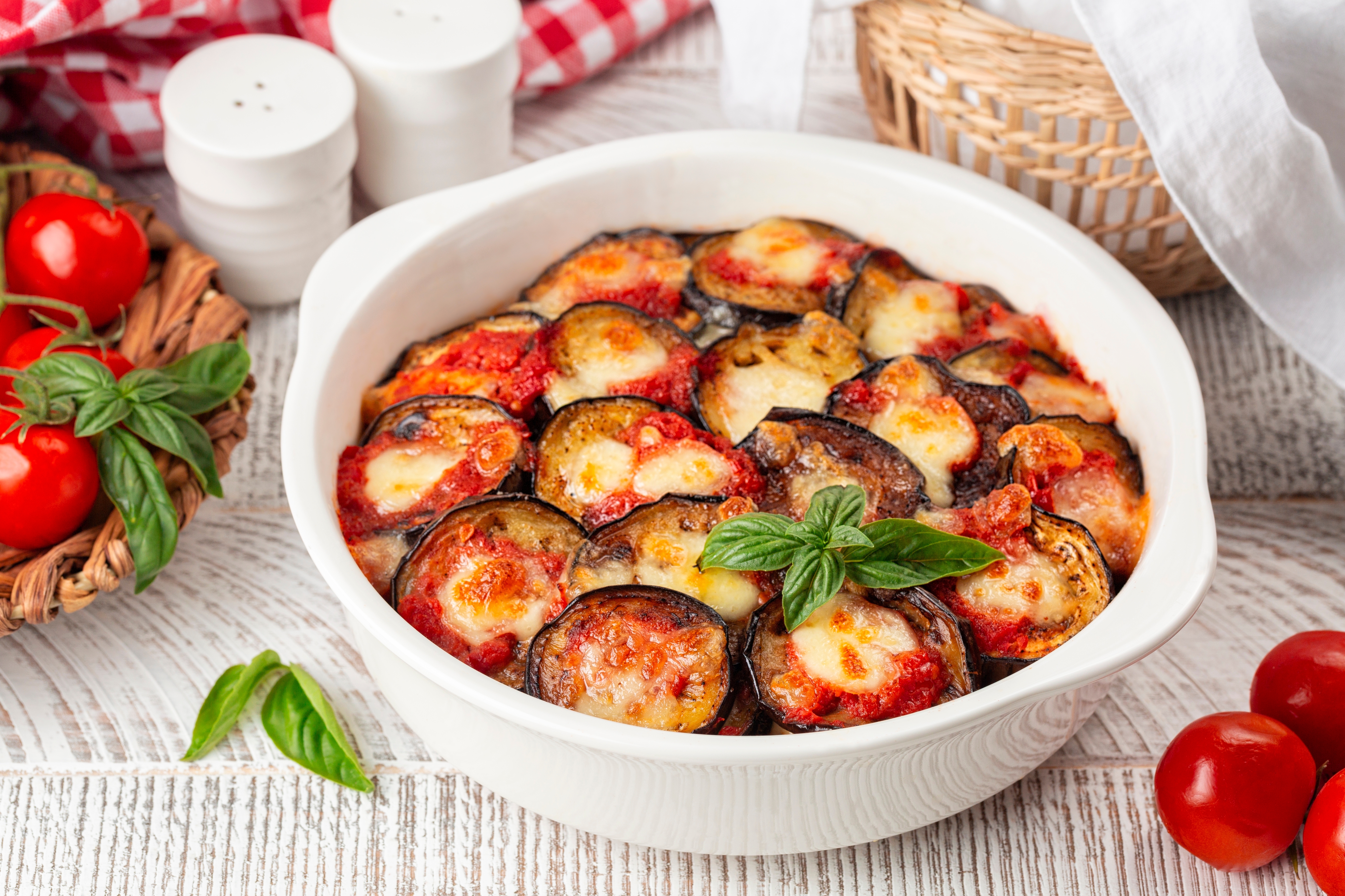 Traditionel italiensk ovnbagt aubergine Parmigiana di Melanzane med mozzarella, tomatsauce og friske basilikumblade serveret i hvid keramikfad