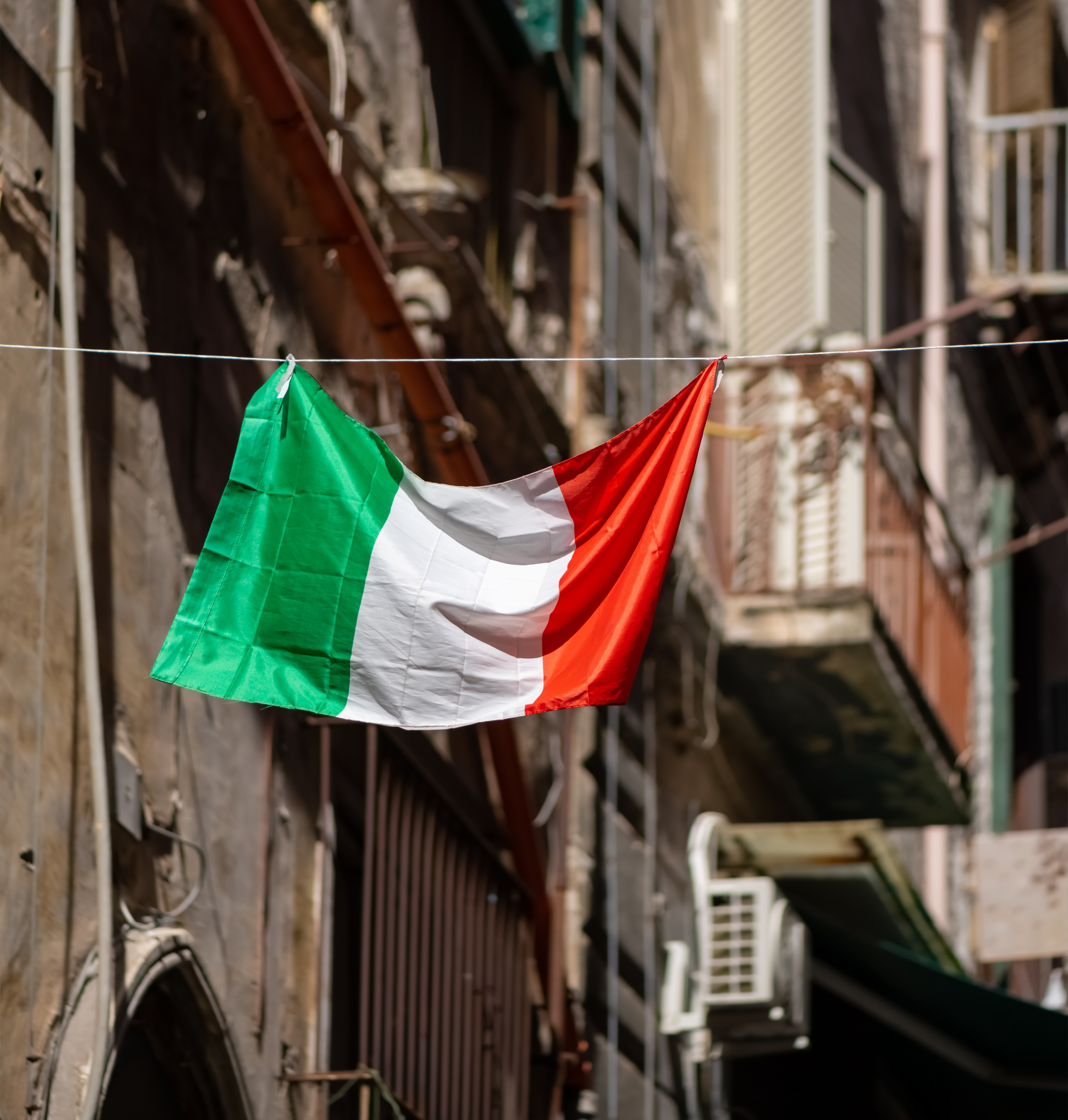 Italiensk flag hænger på tøjsnor i smal gade i Napoli med gamle bygninger