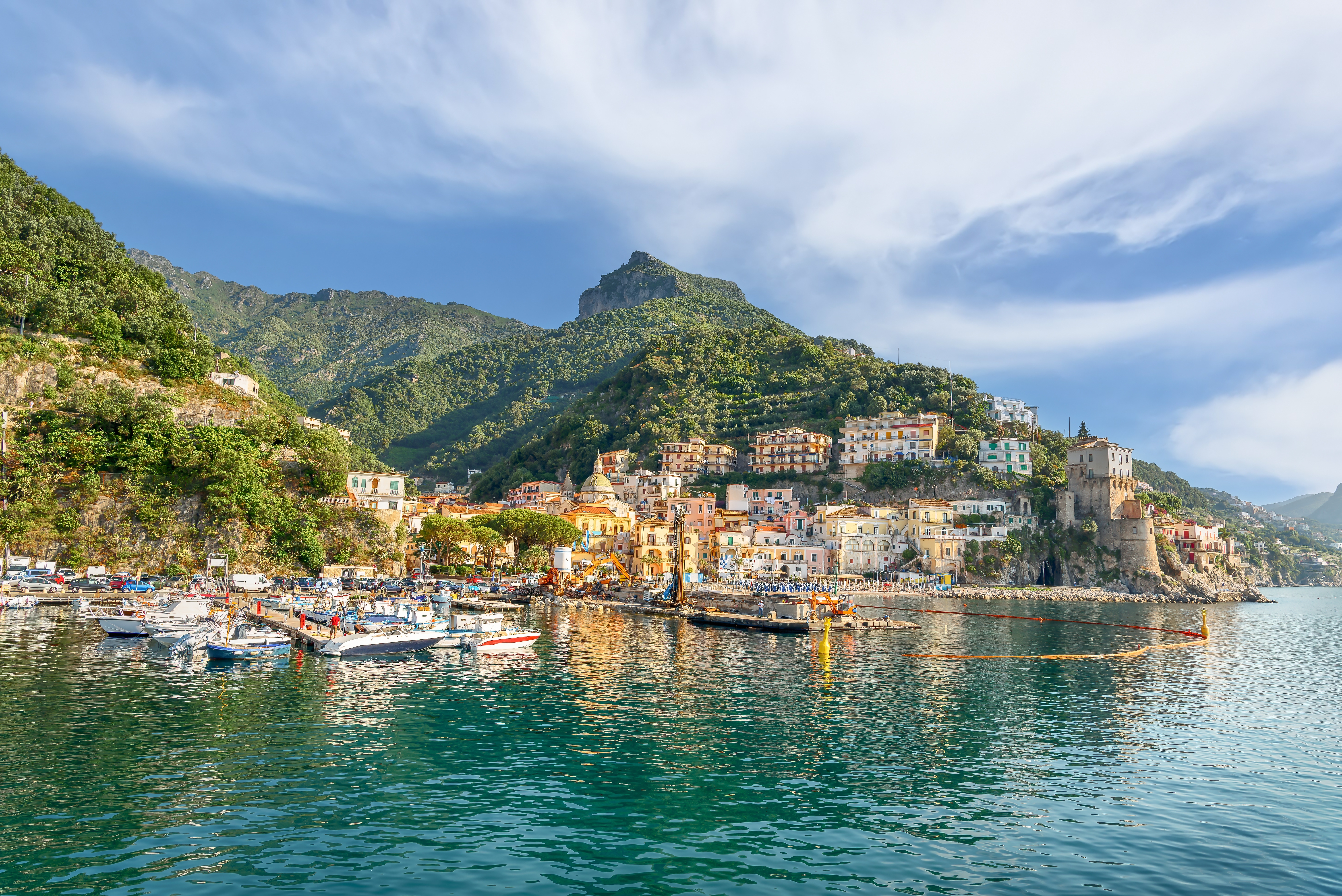 Pittoresk italiensk kystby med farverige huse bygget ind i bjergskråningen og fiskerbåde i havnen ved det turkisblå Middelhav