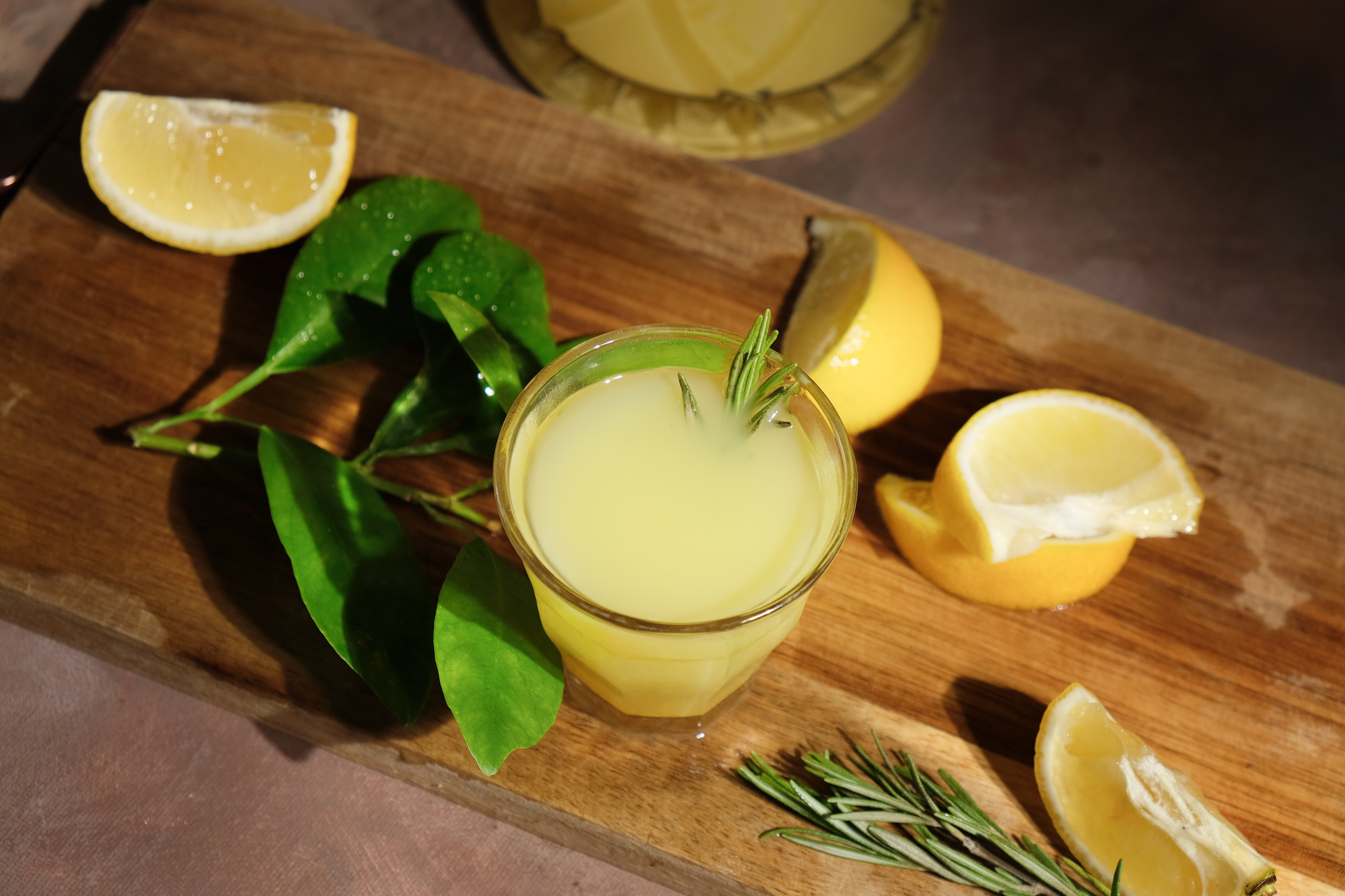 Traditionel italiensk limoncello likør med friske citroner og rosmarin på træskærebræt