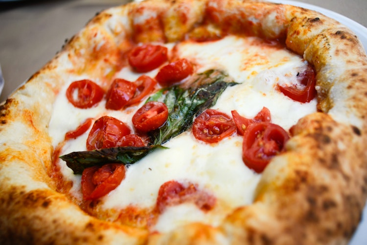 Traditionel italiensk margherita pizza med friske tomater, mozzarella og basilikumblade, serveret på et rustikt træbord under din rejse i Italien