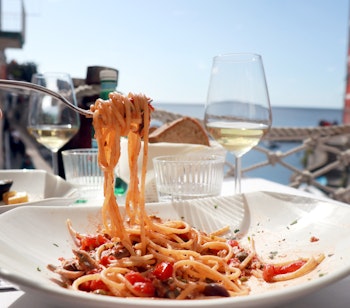 Lækker italiensk pastaret serveret med hvidvin på en eksklusiv restaurant med havudsigt i Cinque Terre, den perfekte kulinariske oplevelse under en sommerferie i Italien