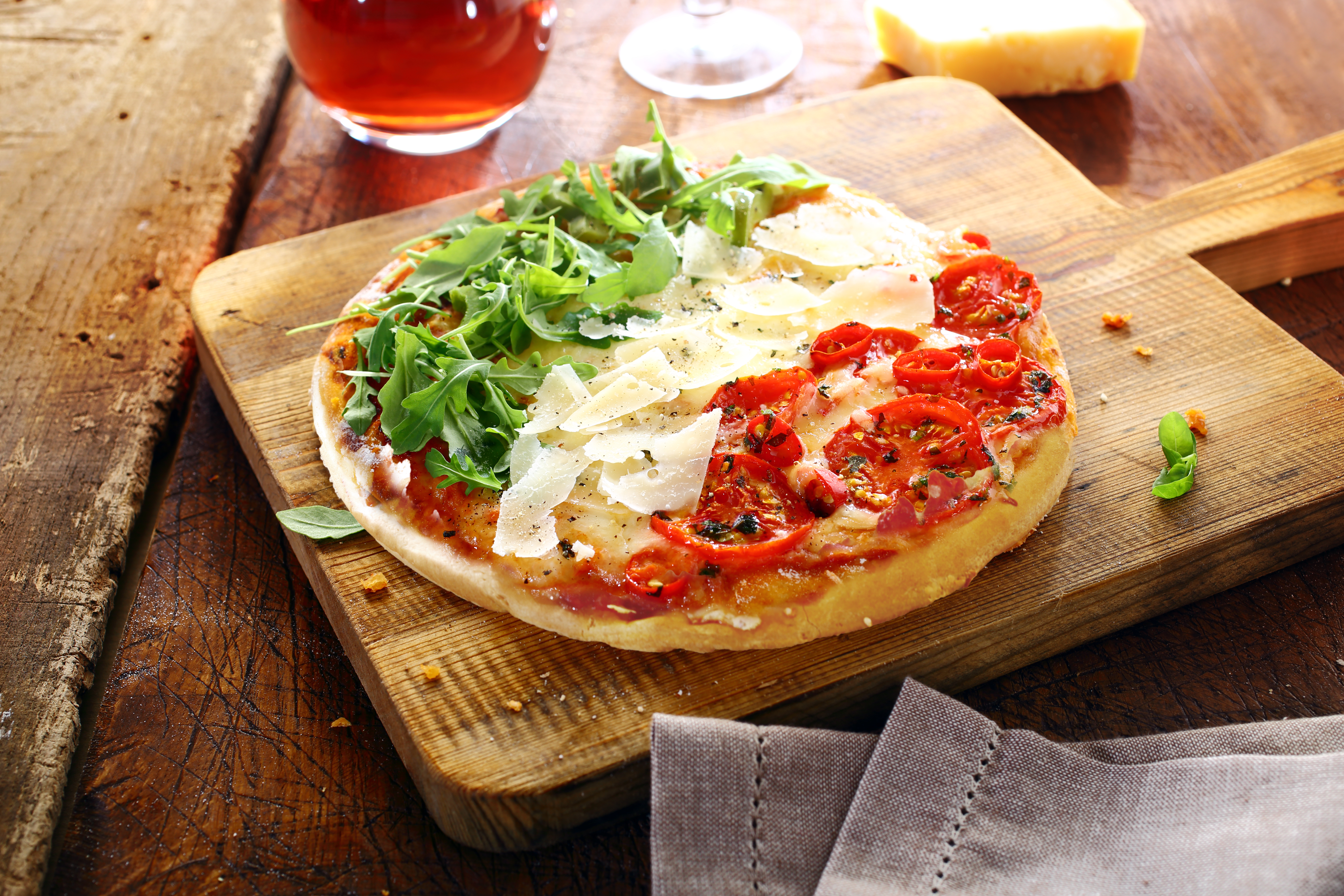 Traditionel italiensk pizza med frisk rucola, cherrytomater og parmesanost på rustikt træbræt