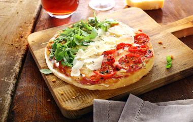 Traditionel italiensk pizza med frisk rucola, cherrytomater og parmesanost på rustikt træbræt